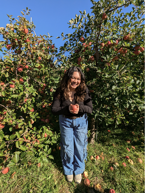 Photo of Amanda smiling holding an apple in front of an apple tree